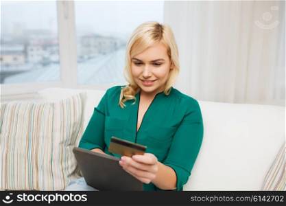 people, internet bank, online shopping, technology and e-money concept - happy young woman sitting on sofa with tablet pc computer and credit card at home