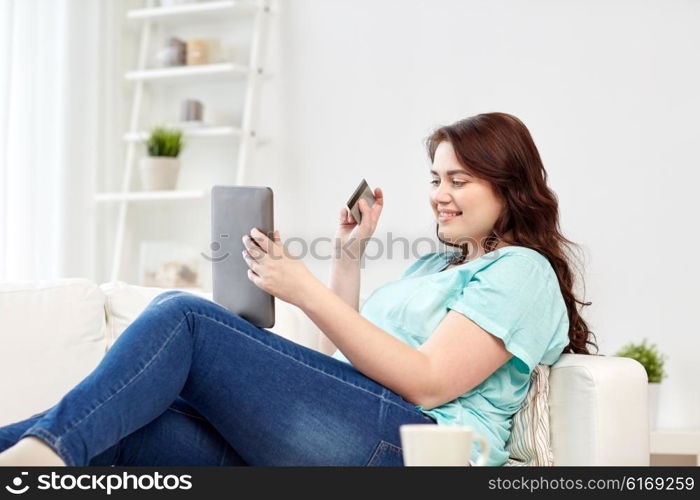 people, internet bank, online shopping, technology and e-money concept - happy young plus size woman sitting on sofa with tablet pc computer and credit card at home