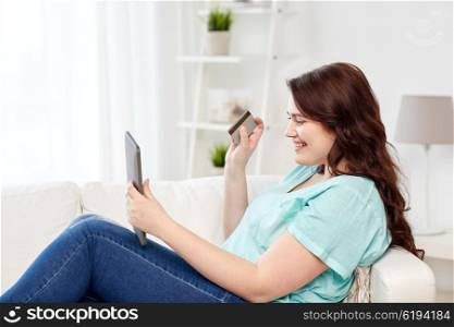 people, internet bank, online shopping, technology and e-money concept - happy young plus size woman sitting on sofa with tablet pc computer and credit card at home
