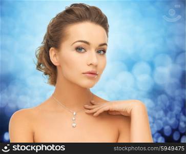 people, jewelry, luxury and glamour concept - woman wearing shiny diamond pendant over blue lights background