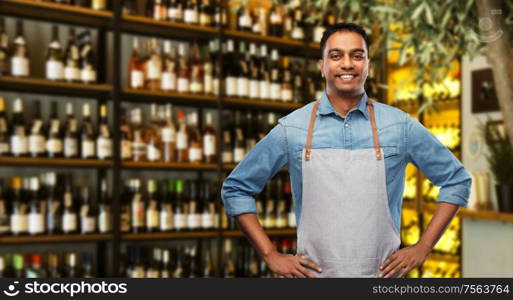 people, job and profession concept - smiling indian barman or waiter in apron over wine bar background. smiling indian barman or waiter at wine bar