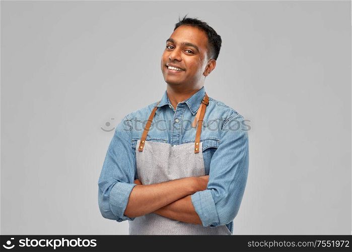 people, job and profession concept - smiling indian barman, waiter or salesman in apron over grey background. smiling indian barman, waiter or salesman in apron