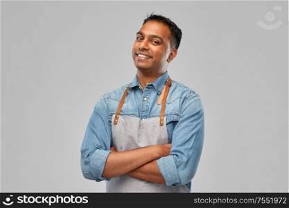 people, job and profession concept - smiling indian barman, waiter or salesman in apron over grey background. smiling indian barman, waiter or salesman in apron