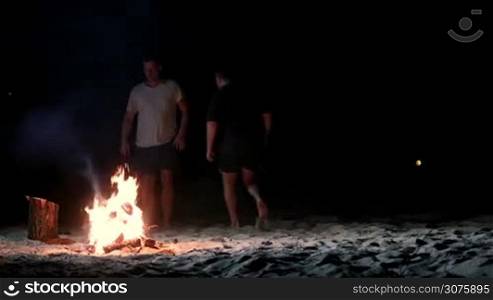 People jumping over bonfire on the beach at night. Smiling friends have fun at night on the beach