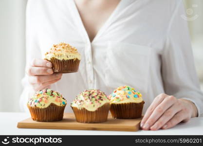 people, junk food, culinary, baking and eating concept - close up of woman with glazed cupcakes or muffins