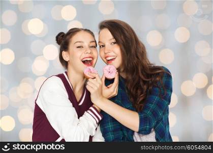 people, junk food, teens and friendship concept - happy smiling pretty teenage girls with donuts eating and having fun over holidays lights background