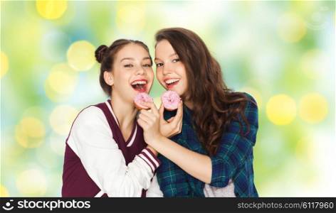 people, junk food, teens and friendship concept - happy smiling pretty teenage girls with donuts eating and having fun over green summer holidays lights background