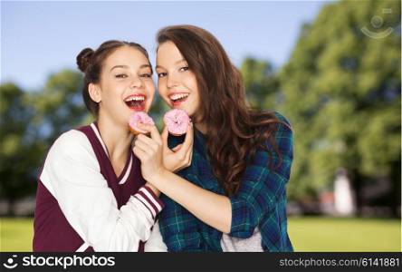 people, junk food, teens and friendship concept - happy smiling pretty teenage girls with donuts eating and having fun over summer park background