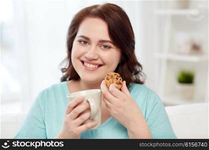 people, junk food, unhealthy eating and leisure concept - happy plus size young woman with cup of tea with cookie at home