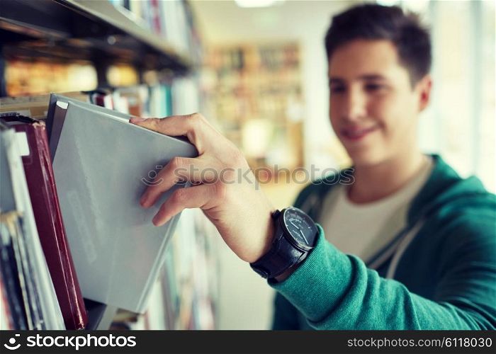 people, knowledge, education and school concept - close up of happy student boy or young man taking book from shelf in library