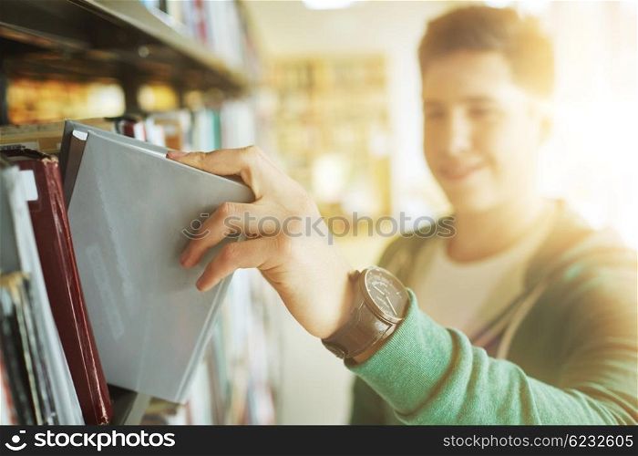 people, knowledge, education and school concept - close up of happy student boy or young man taking book from shelf in library