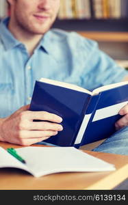 people, knowledge, education and school concept - close up of student reading book at school library