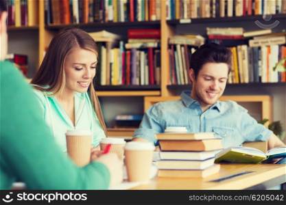 people, knowledge, education and school concept - group of happy students reading books, drinking coffee and preparing to exam in library