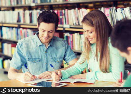 people, knowledge, education and school concept - group of happy students with tablet pc computer writing to notebooks in library