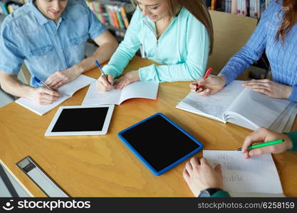 people, knowledge, education and school concept - group of happy students with tablet pc computers writing to notebooks in library