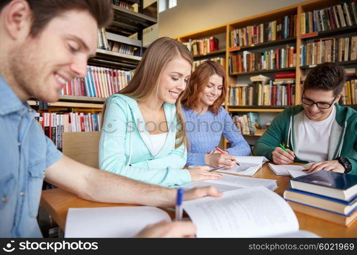 people, knowledge, education and school concept - group of happy students writing to notebooks in library