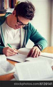 people, knowledge, education and school concept - happy student boy in glasses writing to notebook in library