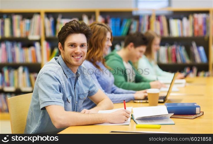 people, knowledge, education and school concept - happy student boy with books writing to notebook in library