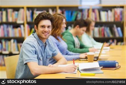 people, knowledge, education and school concept - happy student boy with books writing to notebook in library
