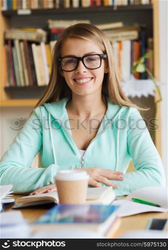 people, knowledge, education and school concept - happy student girl in eyeglasses with book and coffee cup in library