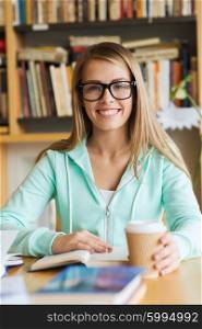 people, knowledge, education and school concept - happy student girl in eyeglasses with book drinking coffee in library