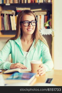people, knowledge, education and school concept - happy student girl in eyeglasses with book drinking coffee in library