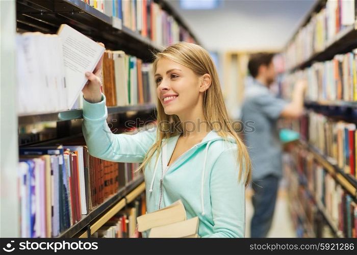 people, knowledge, education and school concept - happy student girl or young woman taking book from shelf in library