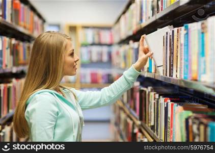 people, knowledge, education and school concept - happy student girl or young woman taking book from shelf in library