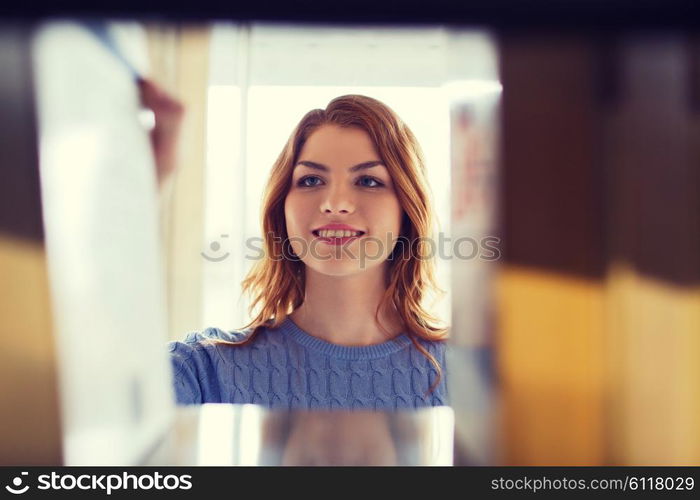 people, knowledge, education and school concept - happy student girl or young woman taking book from shelf in library