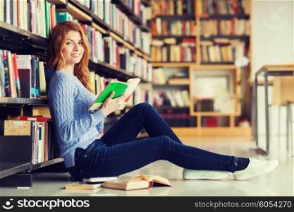 people, knowledge, education and school concept - happy student girl sitting on floor and reading book in library