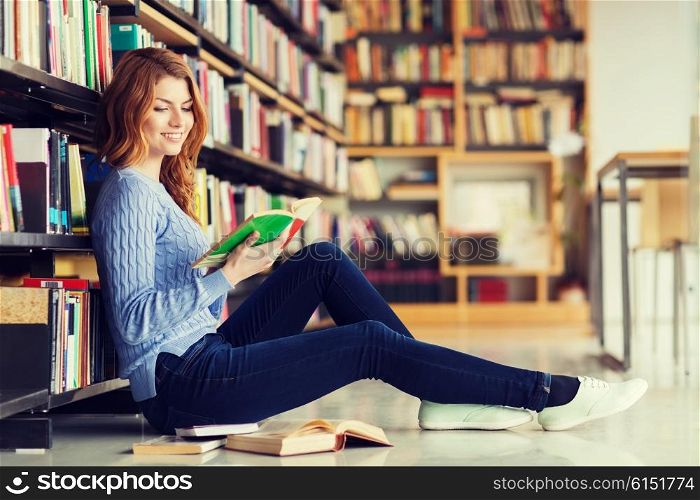 people, knowledge, education and school concept - happy student girl sitting on floor and reading book in library