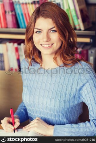people, knowledge, education and school concept - happy student girl writing to notebook in library