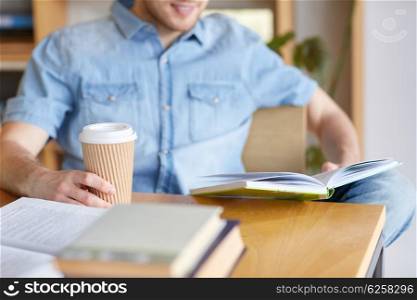 people, knowledge, education and school concept - happy student reading book and drinking coffee in library