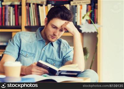 people, knowledge, education and school concept - male student reading book in library