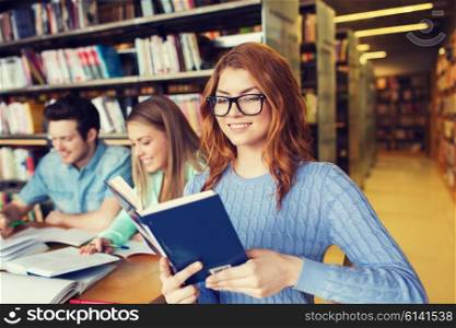 people, knowledge, education, literature and school concept - happy young woman in eyeglasses reading book and preparing to exams over group of students in library