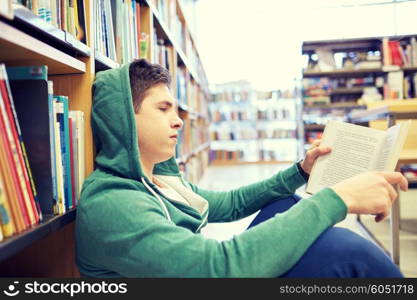 people, knowledge, education, literature and school concept - student boy or young man sitting on floor reading book in library