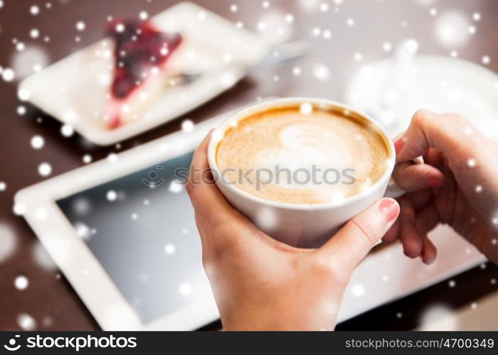 people, latte art, christmas and winter concept - close up of hands with heart in coffee cup, tablet pc computer and cake on table over snow