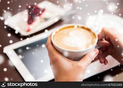 people, latte art, christmas and winter concept - close up of hands with heart in coffee cup, tablet pc computer and cake on table over snow