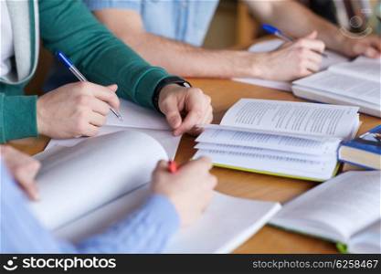 people, learning, education and school concept - close up of students hands with books or textbooks writing to notebooks
