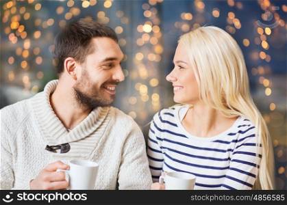 people, leisure and communication concept - happy couple meeting and drinking tea or coffee at cafe over holidays lights