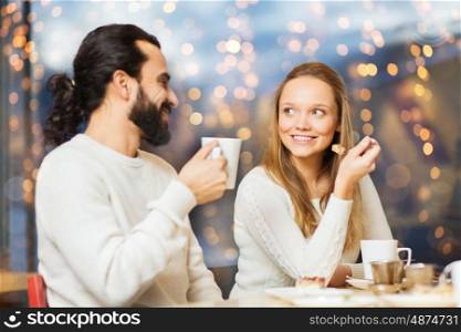 people, leisure and communication concept - happy couple meeting and drinking tea or coffee at cafe over holidays lights background