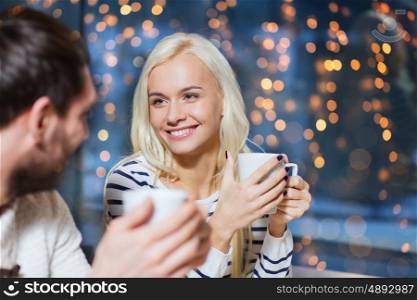 people, leisure and communication concept - happy couple meeting and drinking tea or coffee at cafe over holidays lights