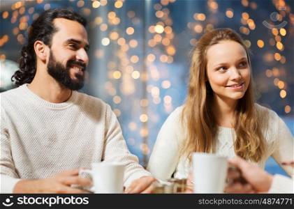people, leisure and communication concept - happy friends or couple meeting and drinking tea or coffee at cafe over holidays lights background