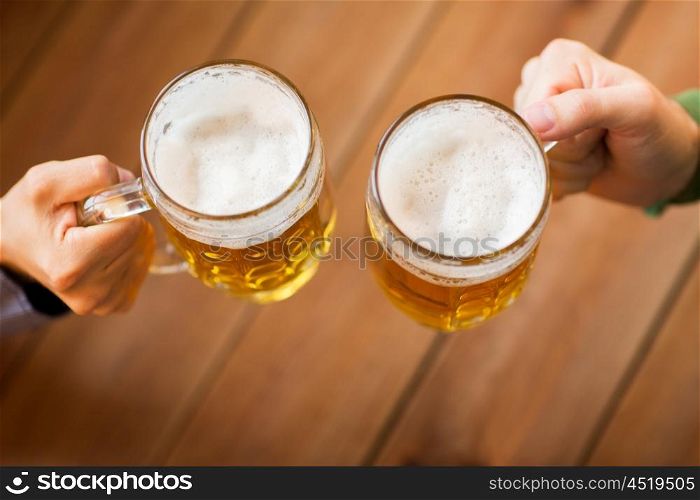 people, leisure and drinks concept - close up of male hands clinking beer mugs at bar or pub