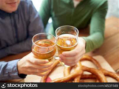 people, leisure and drinks concept - close up of male hands clinking beer glasses and pretzels at bar or pub