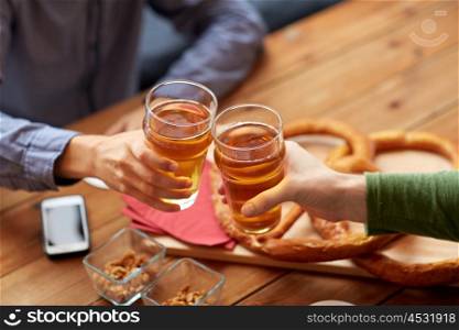 people, leisure and drinks concept - close up of male hands clinking beer glasses and pretzels on table at bar or pub