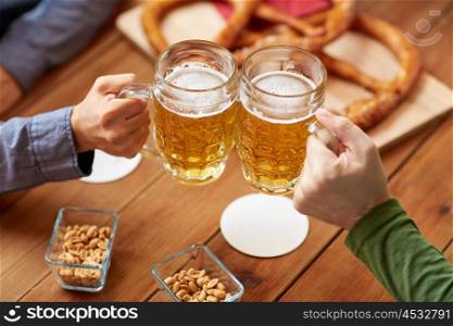 people, leisure and drinks concept - close up of male hands clinking beer mugs and pretzels at bar or pub
