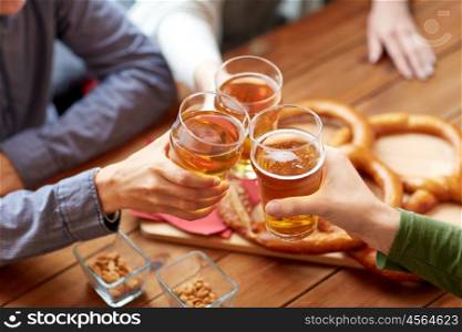 people, leisure and drinks concept - close up of male hands clinking beer glasses and pretzels at bar or pub