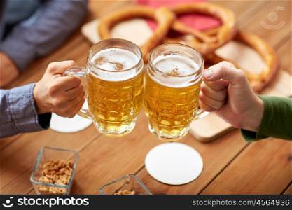people, leisure and drinks concept - close up of male hands clinking beer mugs and pretzels at bar or pub