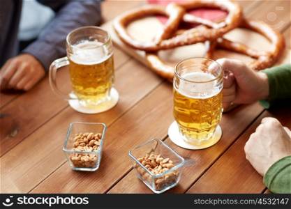 people, leisure and drinks concept - close up of male hands with beer mugs and pretzels at bar or pub
